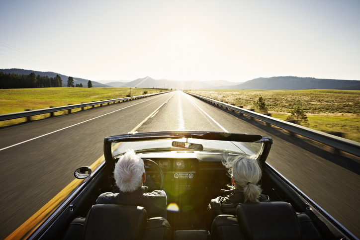 Senior couple driving convertible car at sunrise on rural highway