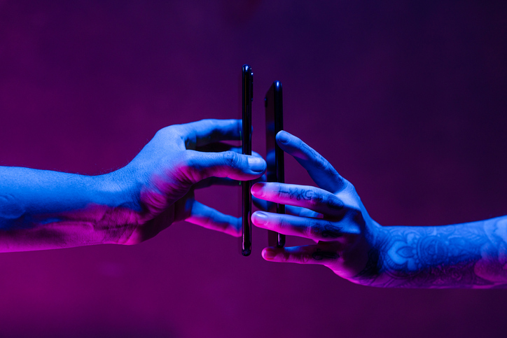 Two people sharing their battery power thanks to wireless charging from one mobile phone to the other. Shot in a studio environment with a futuristic neon lighting.