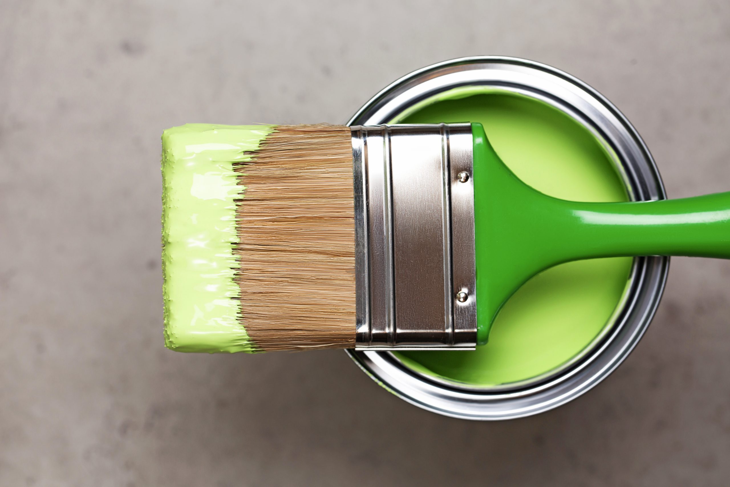 Paintbrush on metal bucket with green pigment for renovation works on concrete gray background. Redecoration concept in home interior. Flat lay style and close-up