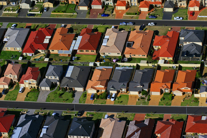 Orange and grey roofs in Sydney's suburbs. This aerial photograph is from a series about Sydney's urban sprawl. The series features the creation of new suburbs, plus infrastructure like roads, parks and power lines. Urban sprawl in Sydney is a contentious issue with opinions divided on the need for the city to expand to house more people, compared to problems of spreading infrastructure and transport too thinly over an increasing area. Housing affordability in Sydney has also become a critical issue with people being unable to afford housing even on the edges of the city.