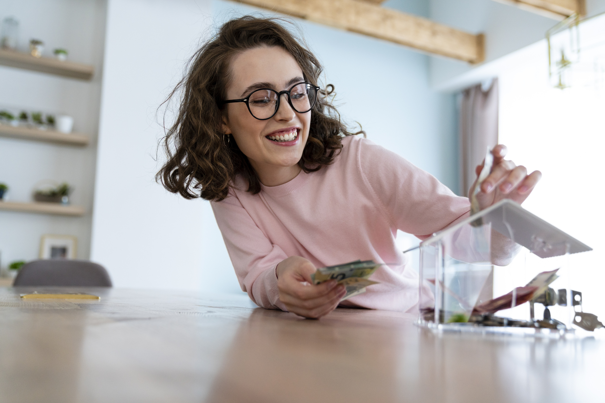 Happy woman saving money in piggy bank at home
